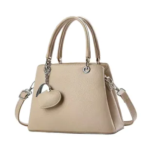 Elegante beige Handtasche mit Litschi-Textur und Herzanhänger auf weißem Grund