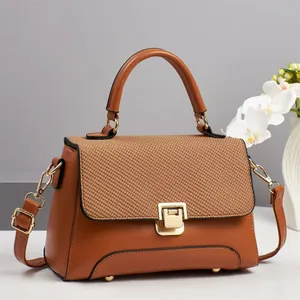 Detail of brown handbag showing woven flap texture and polished gold metal buckle