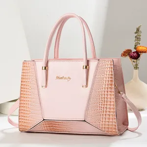 Detail der rosa Handtasche mit Krokodilprägung und goldenem Logo auf glattem Leder