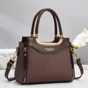 Détail d'un sac à main en cuir marron foncé avec texture rayée et poignée dorée en forme de U