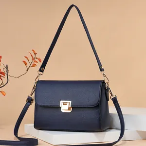 Sac bandoulière minimaliste en cuir bleu marine avec boucle dorée sur un socle blanc