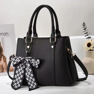 Detail of black pebbled faux leather handbag with a checkered bow and gold metal hardware