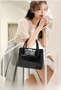 Detail of elegant black crocodile pattern handbag with dual handles and glossy finish