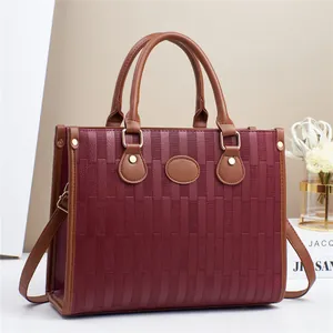 Detail of burgundy woven texture and brown leather trim with golden hardware on tote bag