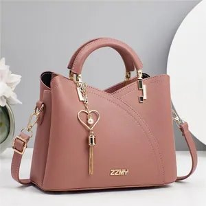 Macro view of dusty pink pebbled leather handbag with gold logo and heart tassel charm