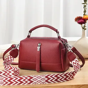 Burgundy faux leather crossbody bag with wide geometric pattern strap on wooden table