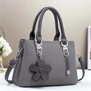 Détail du sac à main gris foncé texturé avec pendentif fleur marron et finitions argentées