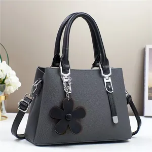 Détail de la texture tricotée d'un sac à main gris foncé avec poignée noire et breloque fleur