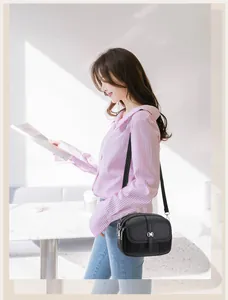 Detail of black pebbled leather crossbody bag with dual zippers and gold buckle