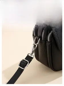 Detail of silver metal hardware hooks and multiple zippers on a black textured leather bag