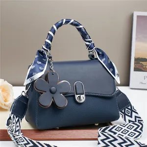 Close-up of navy leather handbag with silk scarf handle and floral charm accessory