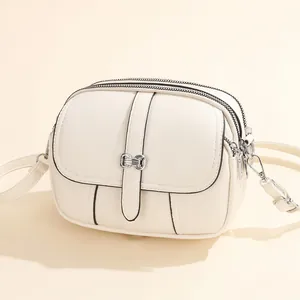 Chic cream mini round crossbody bag with silver bow lock and dual zipper detail