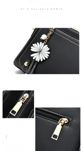 Close-up of black leather handbag with white stitching, daisy charm, and metal zipper
