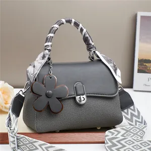 Detail of dark grey tote bag with floral charm, striped scarf handle and patterned strap