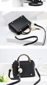 Detail showing black handbag with white stitching, gold hardware and daisy pendant