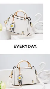 Detail of white leather handbag with golden semicircular handle and daisy charm decoration