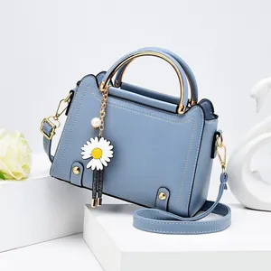 Light blue faux leather crossbody bag with gold handle and daisy charm on white stand