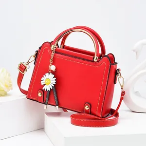 Elegant red square handbag with daisy charm on white display stand, stylish crossbody bag