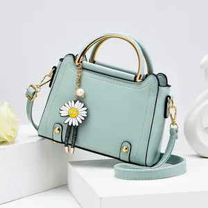 Light blue structured crossbody bag with gold handle and daisy charm on stone stand