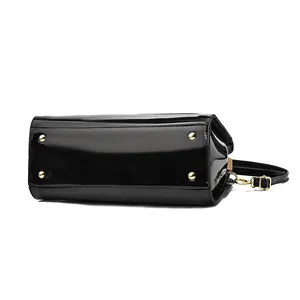 Glossy black patent leather handbag featuring protective gold bottom studs and a shoulder strap