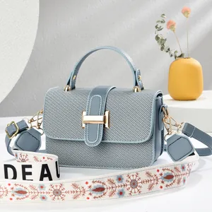 Light blue textured crossbody bag with wide floral shoulder strap and H-shaped gold clasp