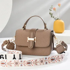 Close-up of brown textured crossbody bag with golden H-buckle and wide embroidered strap