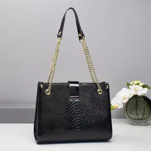 Detailaufnahme der schwarzen Kroko-Handtasche mit goldener Kette und glänzender Schließe