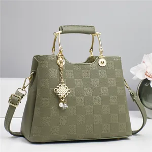 Close-up of olive green checkered handbag with gold metal handle and pearl pendant detail