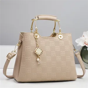 Detail of checkered embossed handbag with gold curved handle and pearl charm pendant