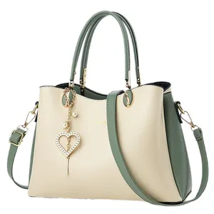 Elegante Tragetasche in Creme und Grün mit goldenem Logo und Herzanhänger