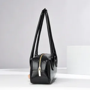 Detail of minimalist black leather shoulder bag with glossy finish and gold metal zipper
