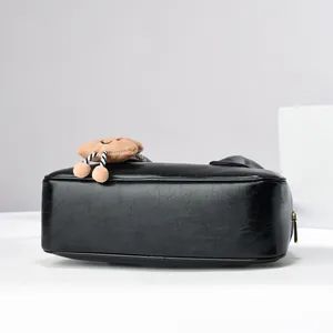 Close-up of black textured leather handbag with a plush brown biscuit keychain charm