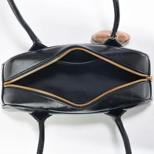 Top view of black leather handbag featuring gold zipper, interior pocket, and plush charm
