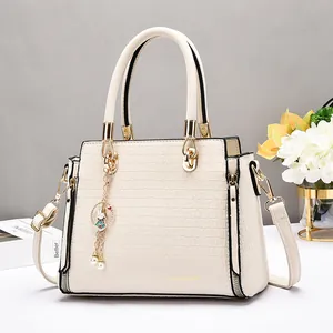 Modische beige Handtasche mit Krokodilprägung, Goldbeschlägen und Hasenanhänger