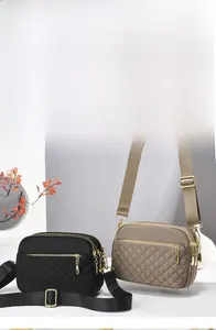 Detail view of khaki and black quilted crossbody bags with multiple gold zipper pockets