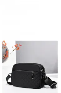 Detail of black quilted shoulder bag featuring multi-zipper compartments and nylon fabric