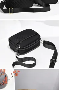 Detail of black quilted crossbody bag showing triple zipper compartments and strap
