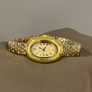 Detail view of oval gold watch with champagne dial and Roman numerals on brown fabric
