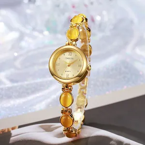 Detalle de reloj dorado con piedras de ojo de gato amarillas y números romanos en la esfera