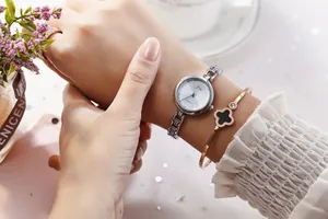 Close-up of a silver quartz watch paired with a rose gold clover bracelet on a wrist