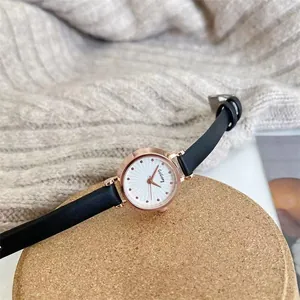 Elegant rose gold women's watch with white dial and slim black leather strap on cork