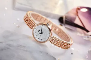 Détail du bracelet perlé en or rose et cadran argenté scintillant sur fond de marbre