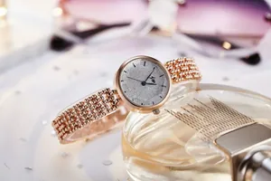 Détail de montre à bracelet perlé or rose et cadran scintillant sur un flacon de parfum