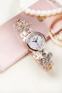 Macro shot of rose gold floral quartz watch with crystals and white dial on a pink background