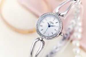 Detail of silver ladies watch featuring a crystal bezel and blue hands on white dial