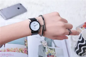 Close-up of minimalist black leather watch with round white dial and nail design jewelry