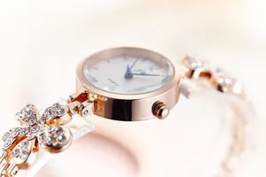Detailed close-up of rose gold watch band with crystal-encrusted floral links and white dial