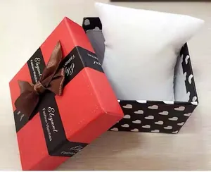 Detail view of a square watch gift box with red lid, ribbon bow, and soft white watch pillow