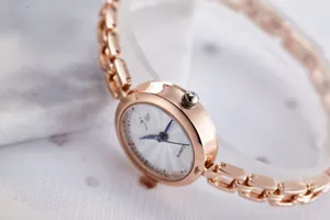 Close-up of elegant rose gold round dial watch with metal chain strap on marble