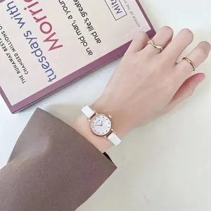 Detail of white leather strap watch with gold case on wrist with gold rings